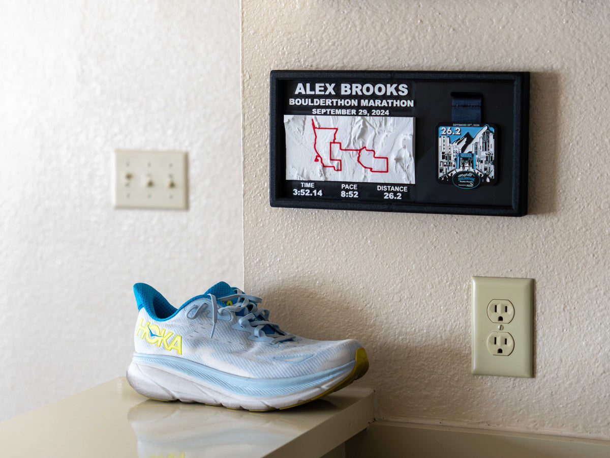 Custom 3D race course medal display on a wooden surface, showing a marathon route with its hills, the runner's finish time, pace and distance, and the finisher medal hanging on the right